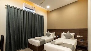 A hotel room with two single beds, a wooden headboard, a nightstand, and a large window with curtains. - Saravana Grand Suites – A Unit of Saravana Bhavan Veg Tables Kochi (Kanayannur)