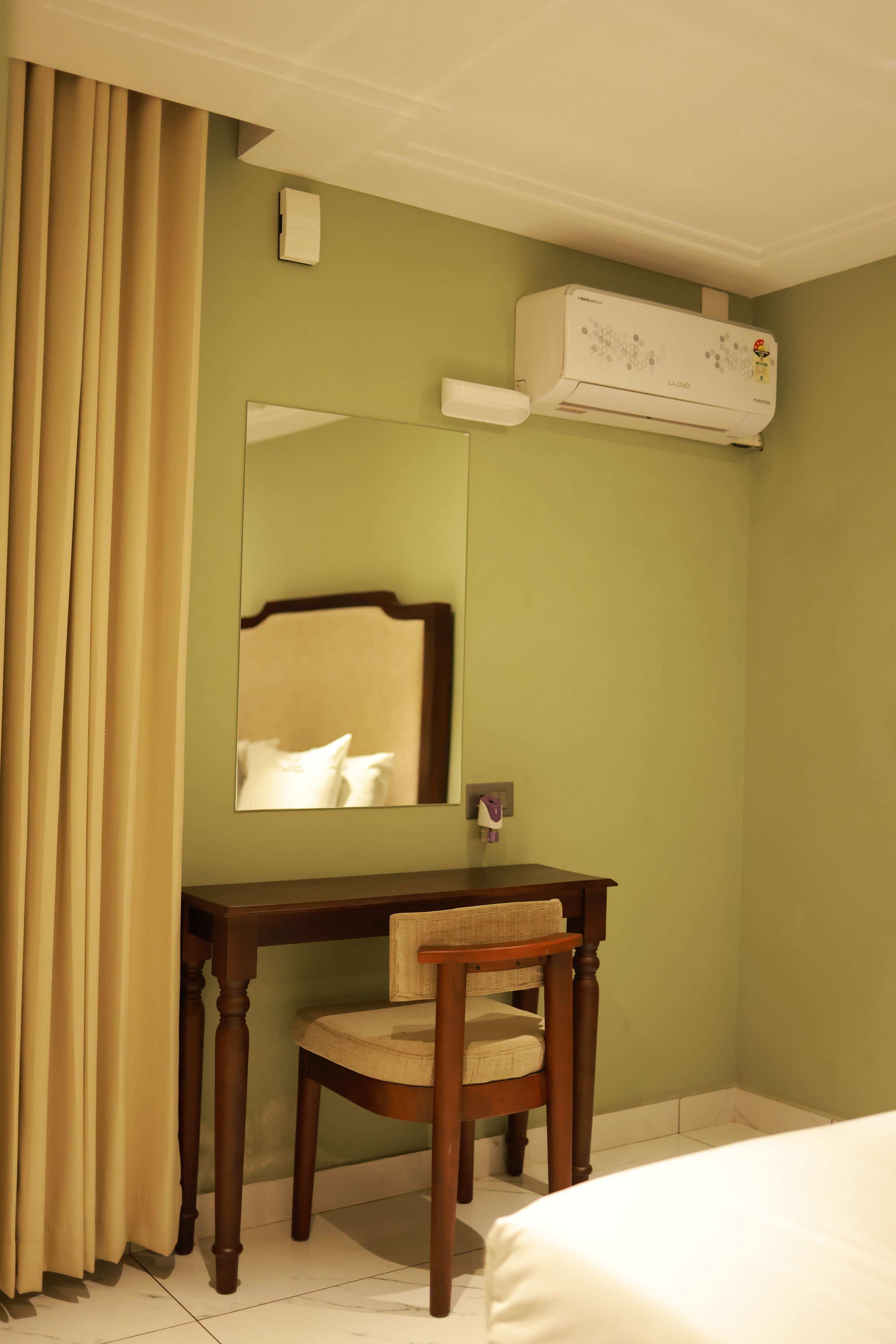Habitación de hotel con escritorio de madera, una silla, una cama, un espejo y un equipo de aire acondicionado.