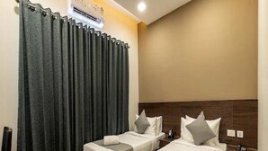 Een hotelkamer met twee bedden, een houten hoofdbord, een nachtkastje en een wandairconditioner.