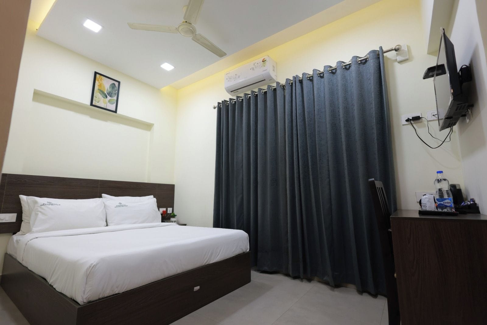 A hotel room with a bed, a ceiling fan, an air conditioning unit, a television, and a curtain.