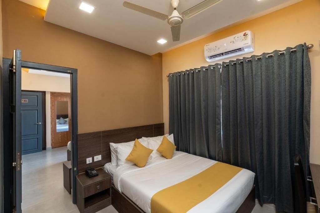 A hotel room with a bed, bedside table, nightstand, and an air conditioning unit on the wall.