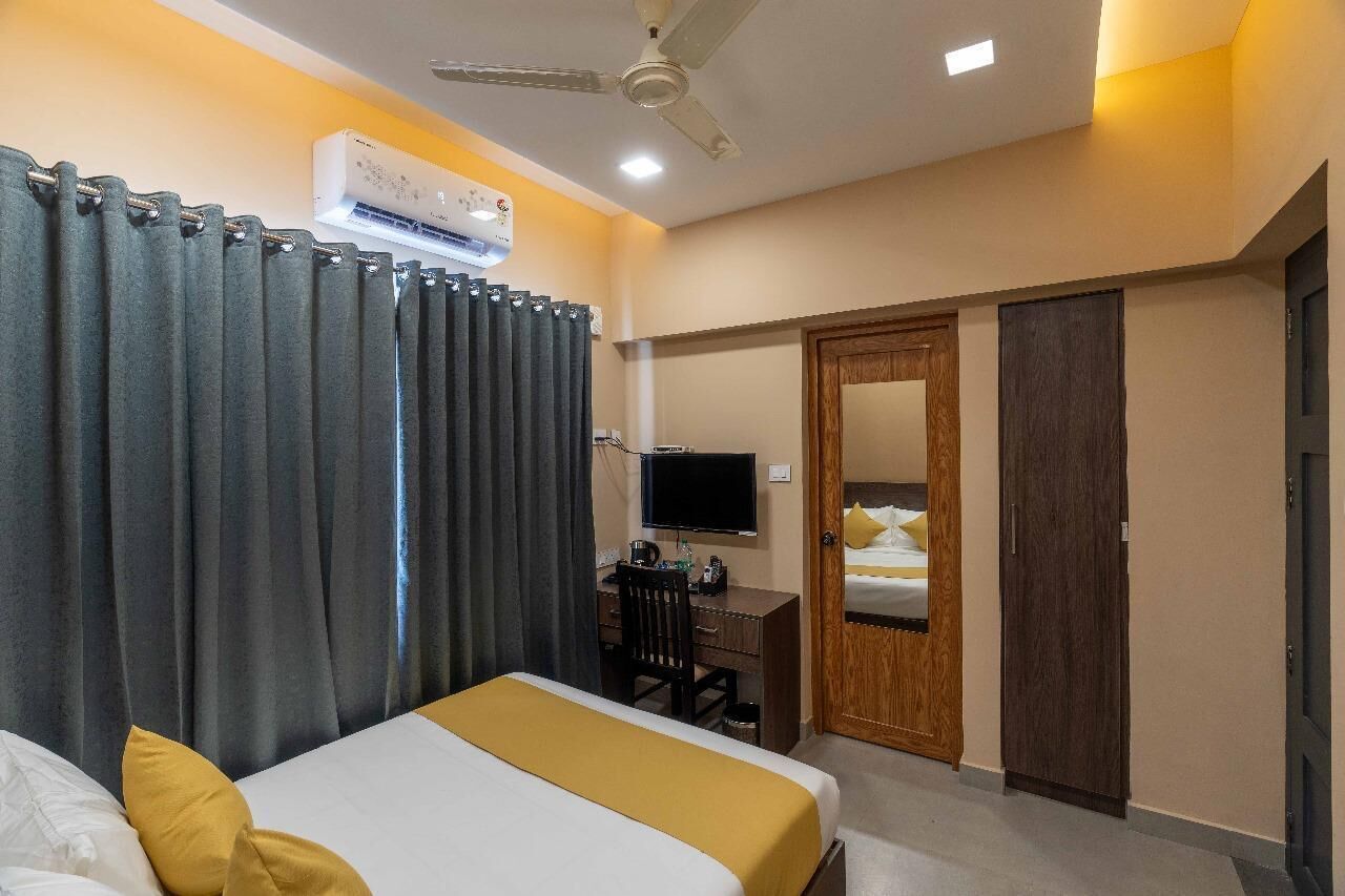 A hotel room with a bed, a desk with a computer, a television, a wardrobe, and a ceiling fan.
