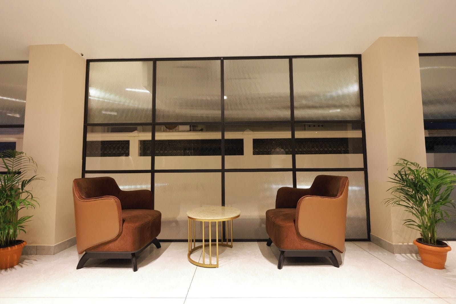 A seating area with two chairs and a small round table, positioned in front of a large window with a metal grid.