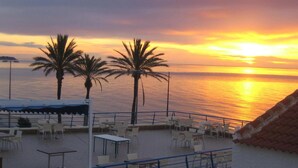 Une terrasse avec des tables et des chaises, des palmiers et une vue sur le coucher de soleil.