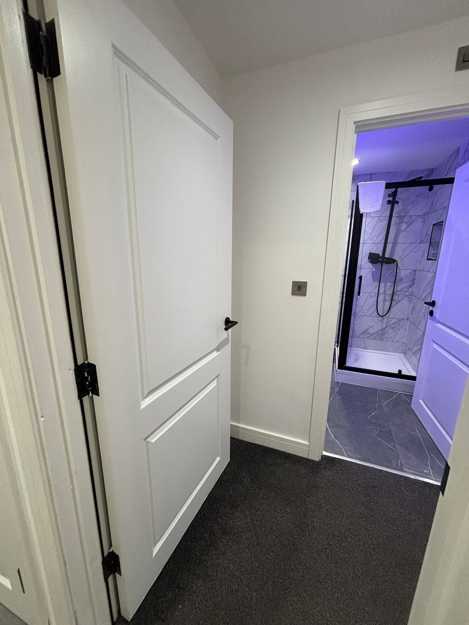 A hallway leading to a bathroom with a shower and a door with a black handle.