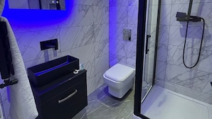 A modern bathroom with a glass shower enclosure, a black vanity, and a white toilet. - Aurora Apartments (Peterborough)