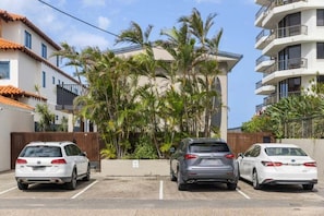 Een parkeerplaats met drie auto's, een gebouw met balkons en palmbomen.