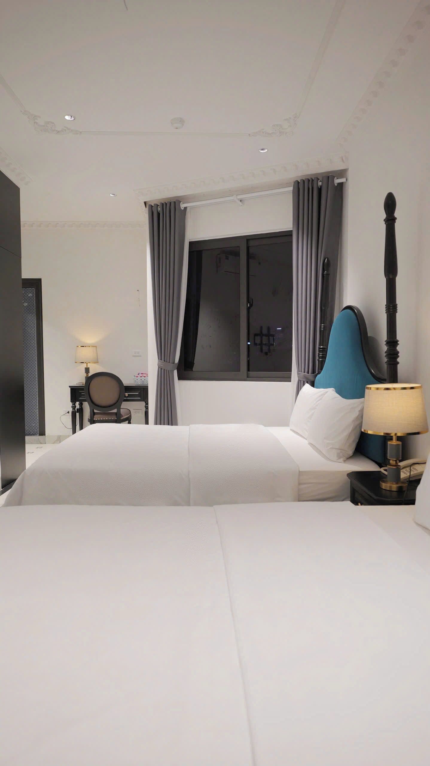 A modern bedroom with a large bed, a desk with a chair, and a window with curtains.