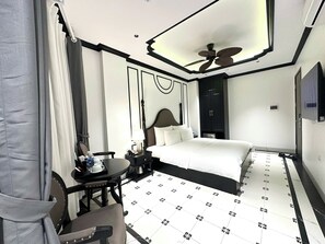 A hotel room with a bed, a desk with a chair, a desk lamp, a telephone, a water bottle, a cup, and a ceiling fan. - Royal Hotel Trinh Van Bo Nam Tu Liem (Hanoi)