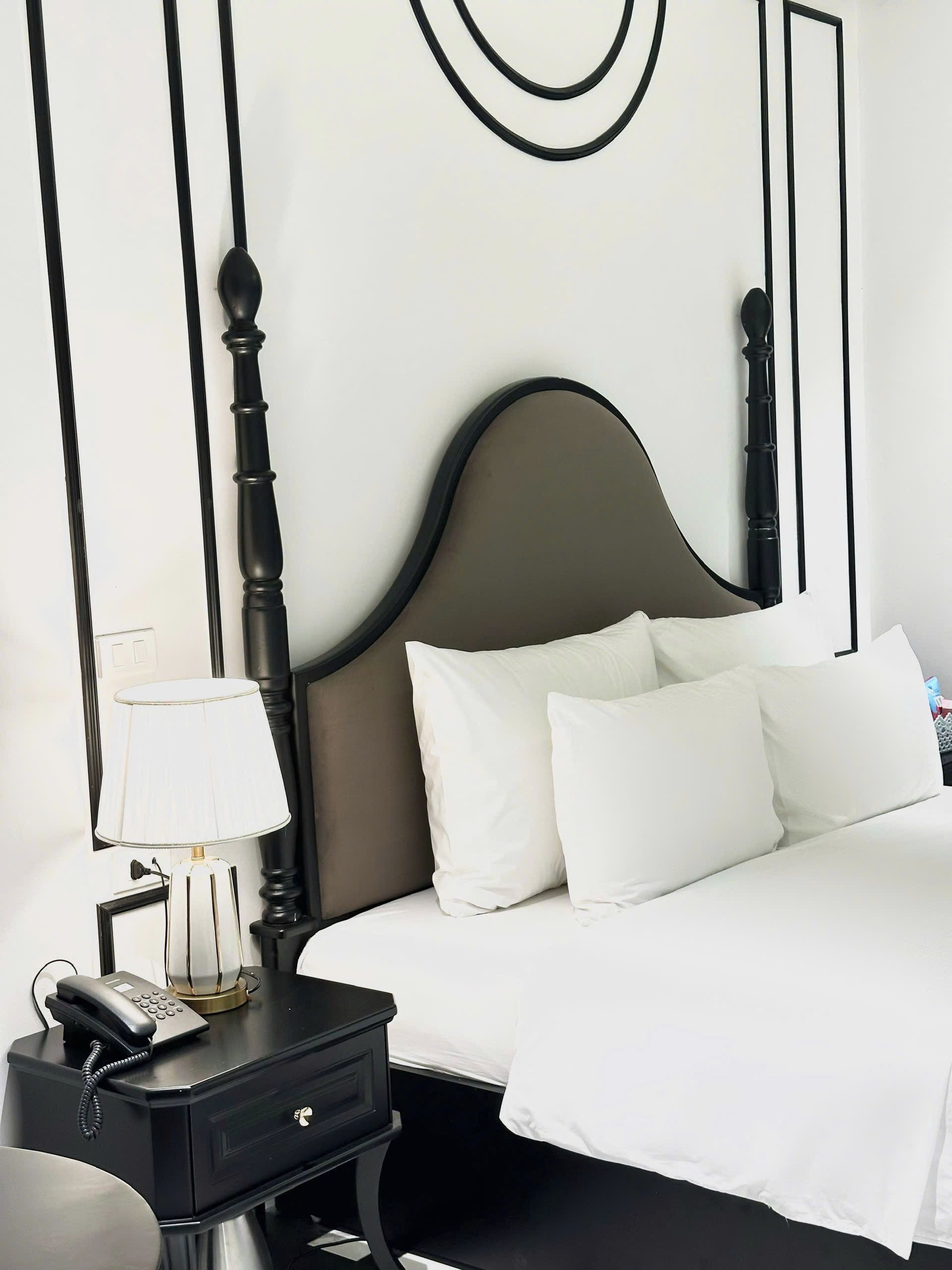 A neatly made bed with white linens, a bedside table with a lamp, and a telephone.