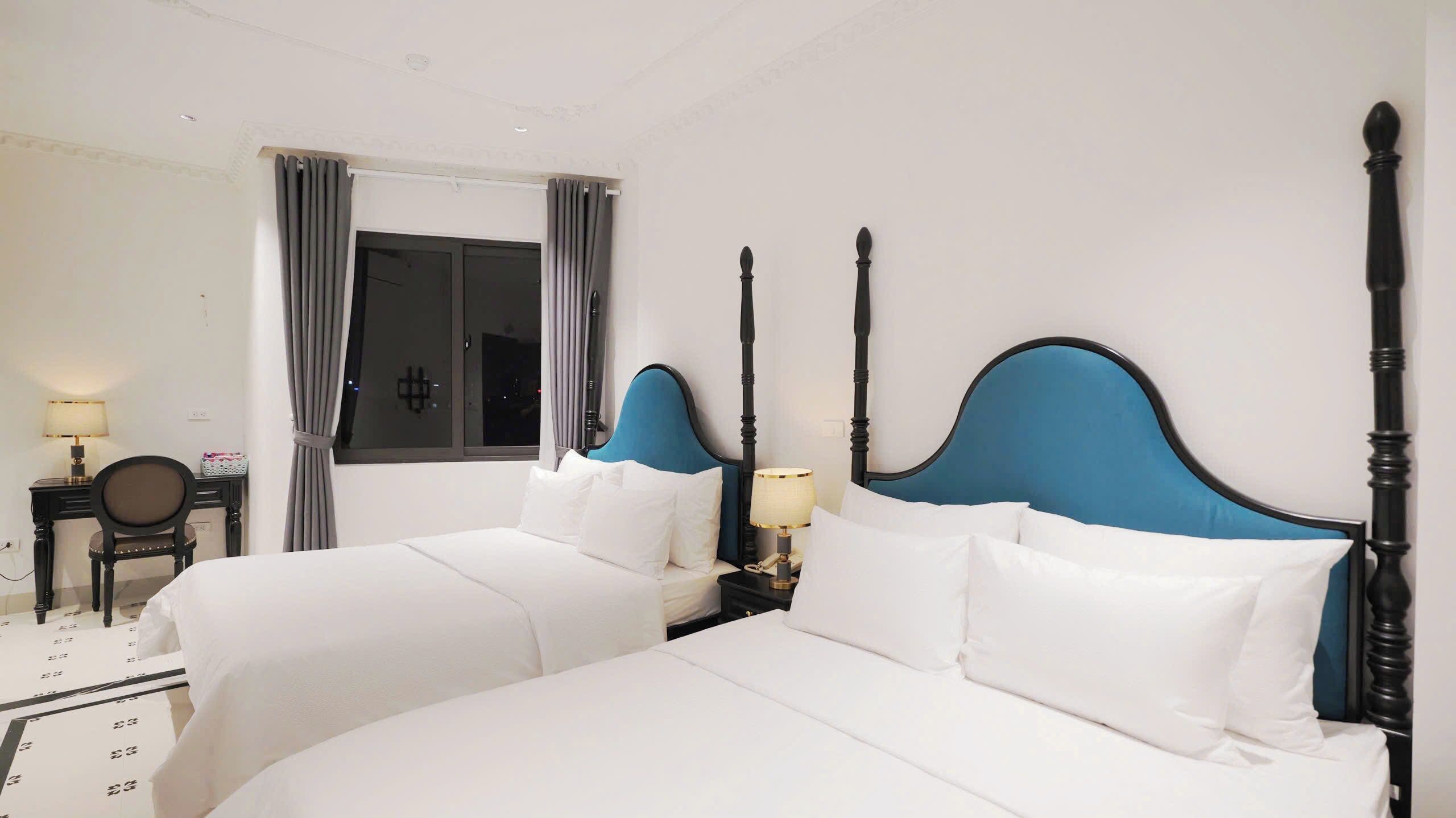 A hotel room with two beds, a desk with a chair, and a window with curtains.