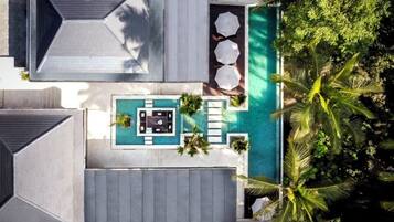 An aerial view of a modern house with a swimming pool, outdoor seating, and lush greenery.