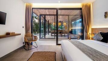 A modern hotel room with a large bed, a flat-screen TV, a dining area with a table and chairs, and a sliding glass door leading to a balcony.