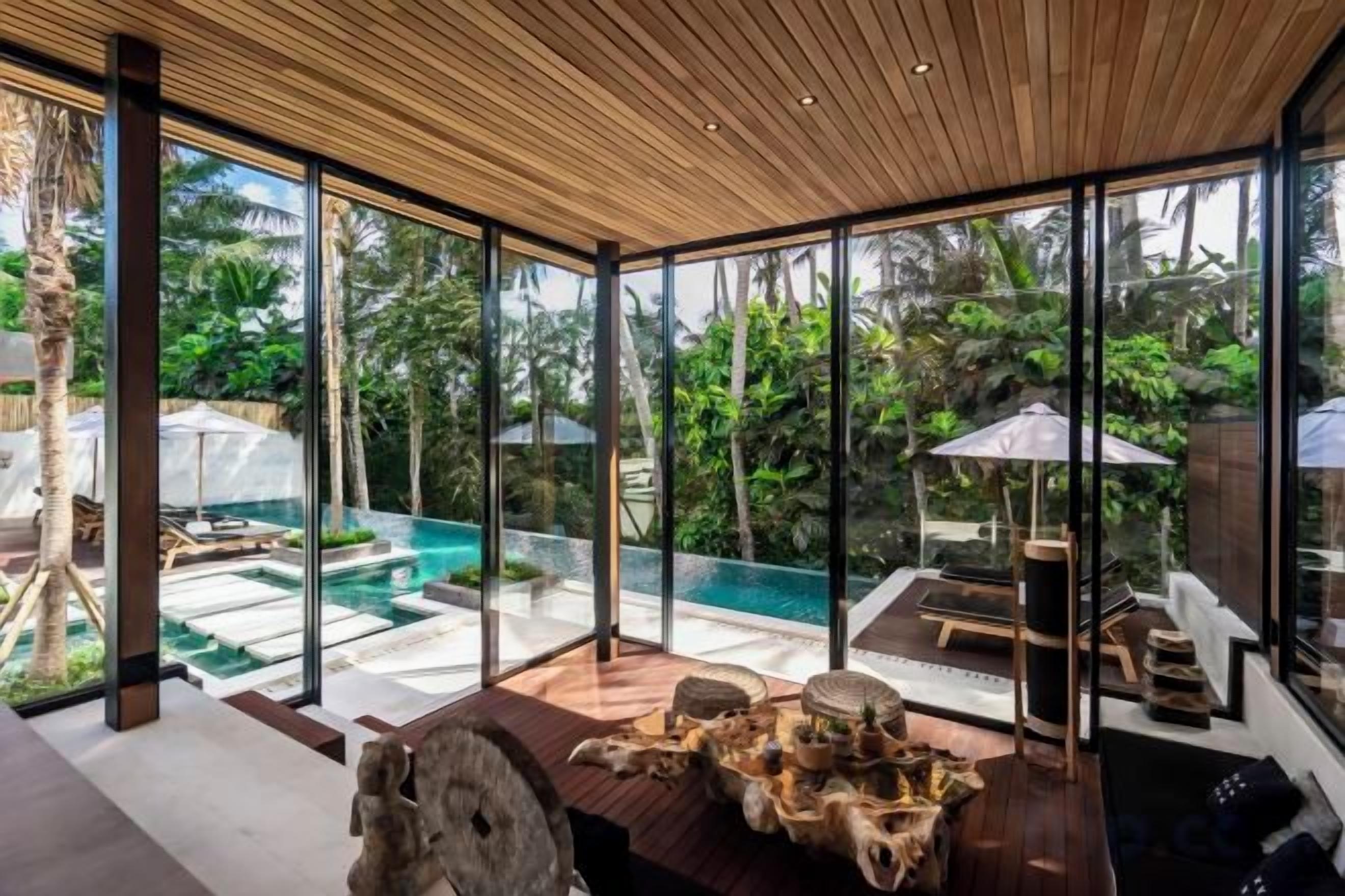 A modern interior with a glass wall overlooking a pool and lush greenery.