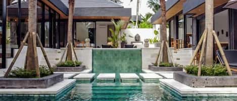 Un área de piscina moderna con agua cristalina, rodeada de palmeras y arquitectura contemporánea.