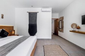 A bedroom with a bed, bedside table, wall-mounted air conditioning unit, and a hanging textile. - Villa Maya Bay by BaliSuperHost (Bali)