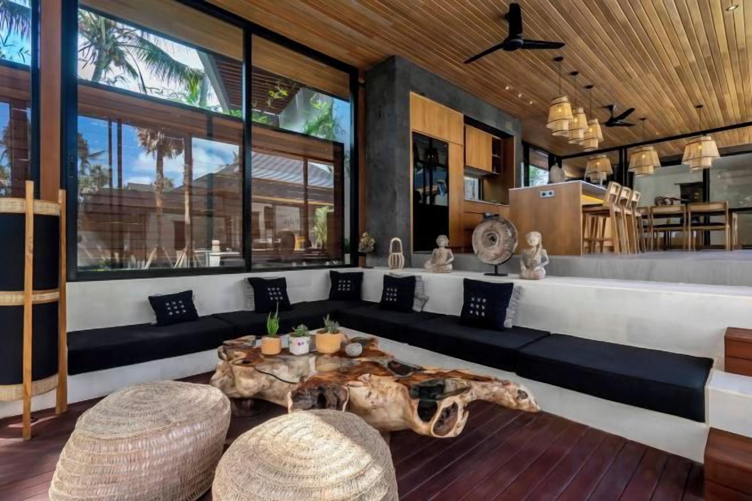 A modern interior with a wooden ceiling, large windows, a seating area with cushions, and a unique coffee table.