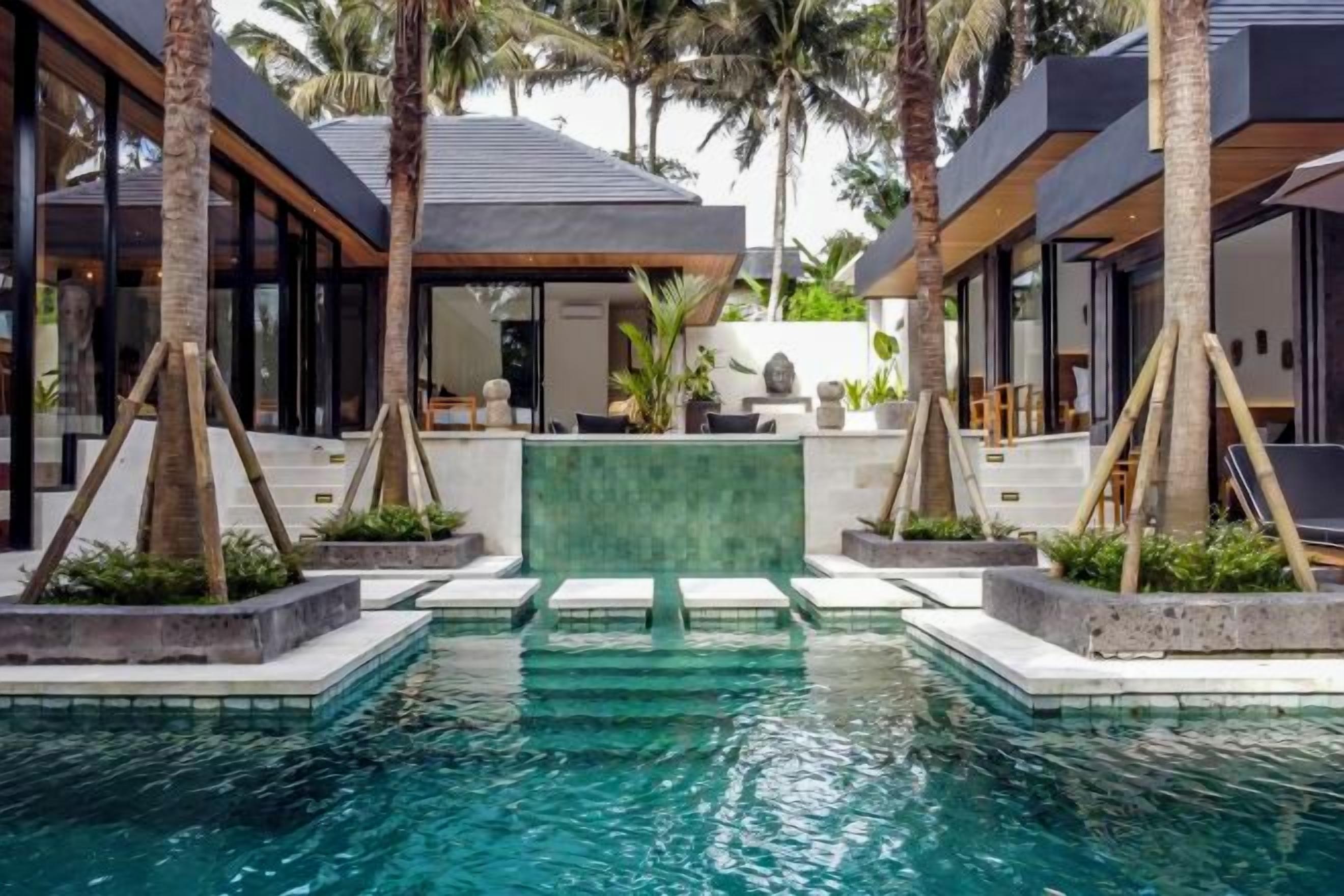A modern pool area with a geometric water feature, surrounded by palm trees and contemporary architecture.