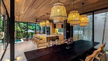 A modern dining area with a large wooden table, wicker pendant lights, and a view of the outdoors.