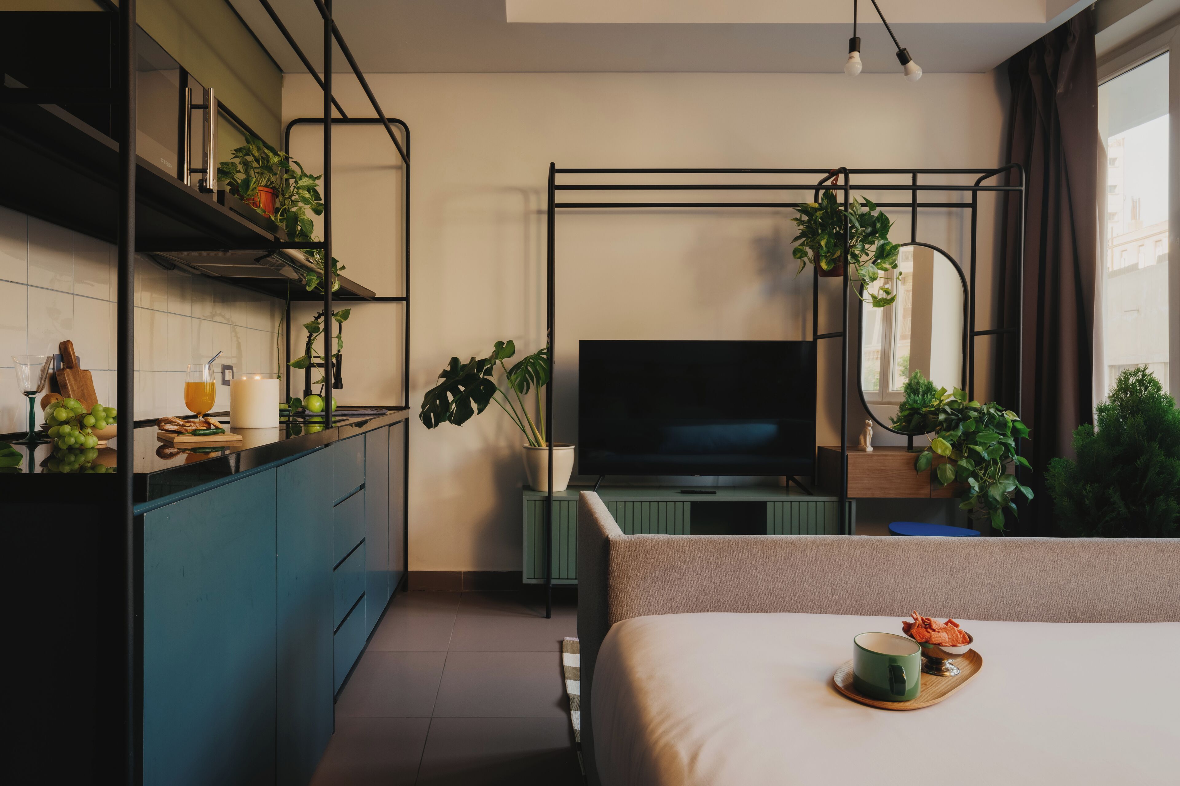 A modern kitchen with a flat-screen TV, a dining area with a table set for two, and a bed with a tray of food.