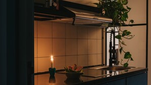 A kitchen with a tiled backsplash, a stainless steel sink, a black countertop, a lit candle, and a potted plant. - Brassbell | DT | Hannaux | Tahrir Sq (Cairo)