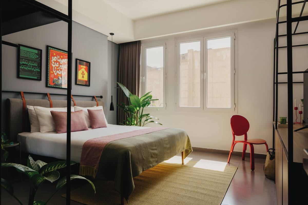 Ein modernes Schlafzimmer mit einem Bett, einem roten Sessel, einem Fenster und Wandbildern.