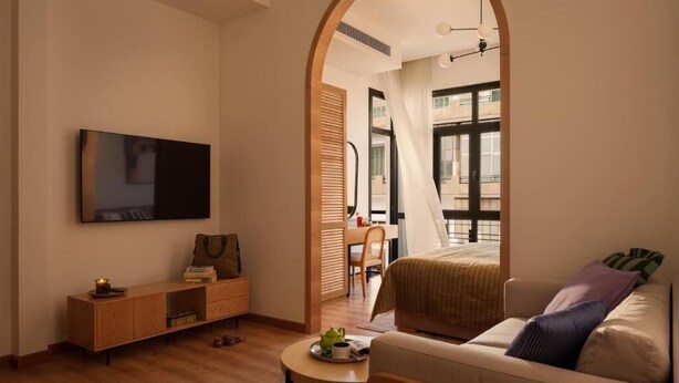 A modern hotel room with a flat-screen TV, a wooden console table, a sofa with cushions, a small round table with a cup and saucer, and a large window with a view of the outside. - Brassbell | DT | Hannaux | Tahrir Sq (Cairo)