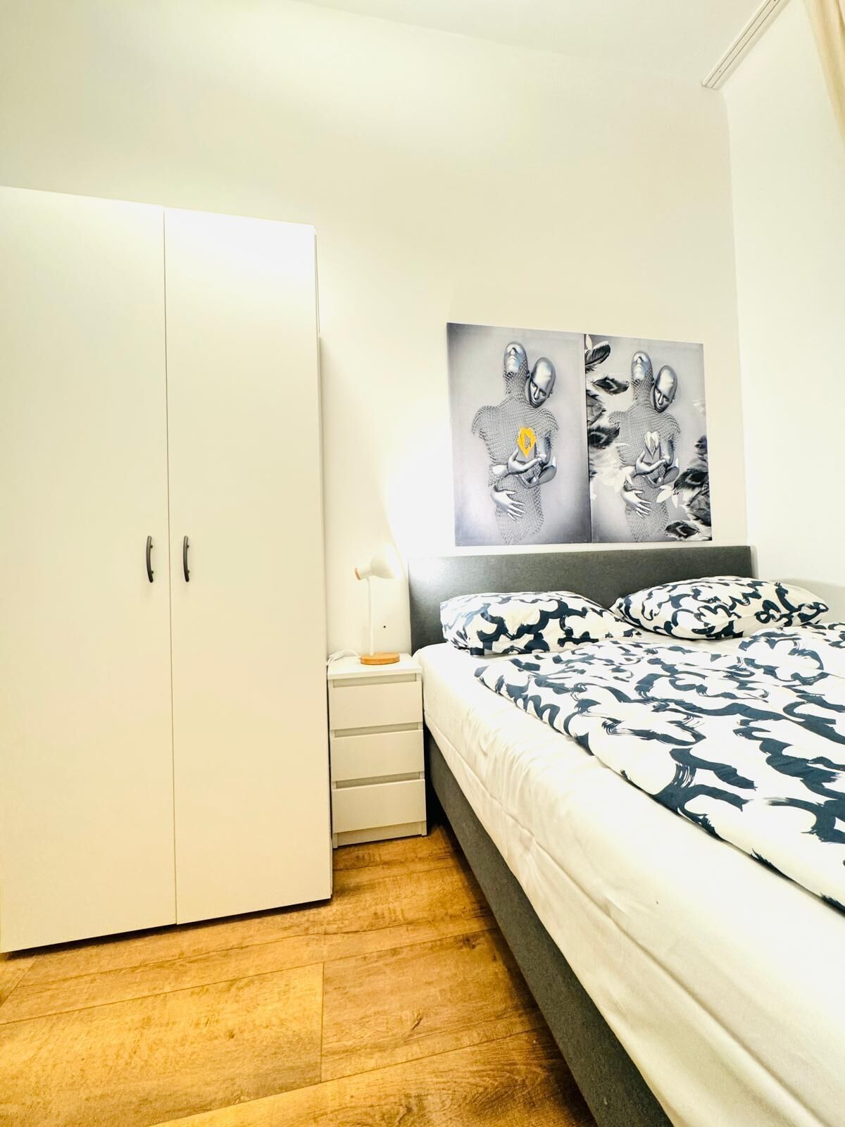 A bedroom with a bed, a wardrobe, a nightstand, and a wall-mounted artwork.
