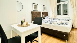 Una habitación compacta con una cama individual, una mesita con una silla, una lámpara de noche y una ventana con cortinas.