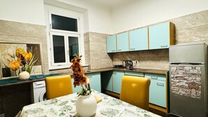 Una cocina compacta con armarios color esmeralda, un refrigerador con frente de piedra y un comedor con una mesa dispuesta para dos.