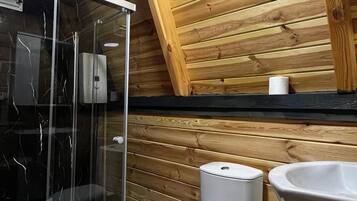 Ein kleines, modernes Badezimmer mit Holzboden, einer Glasdusche, einer weißen Toilette und einem Waschbecken mit rotem Wasserhahn.