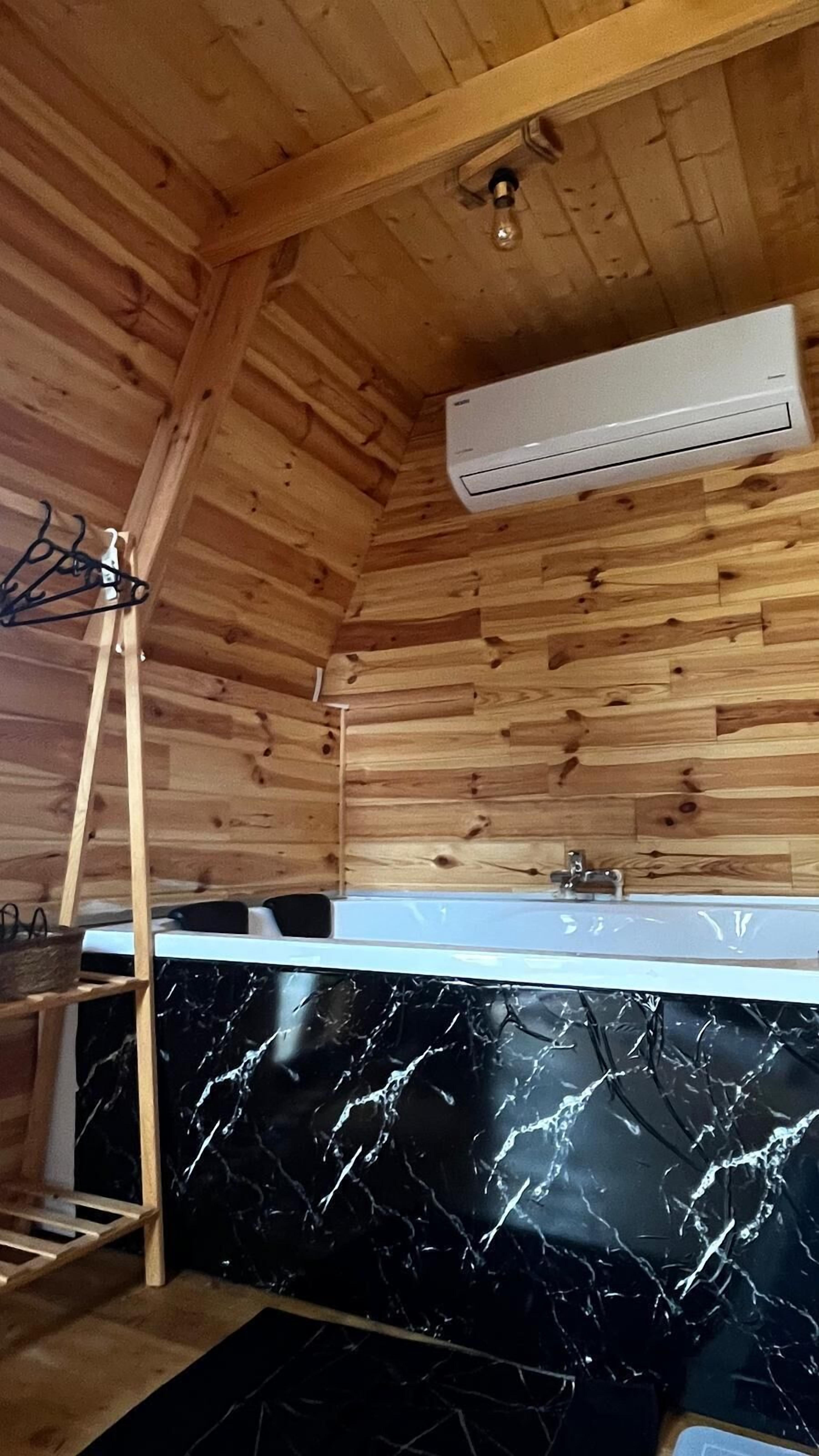 Interior de una cabaña de madera con lavamanos de encimera de mármol, una escalera y un equipo de aire acondicionado.