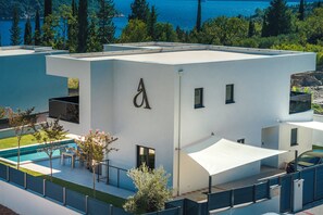 A modern building with a pool, outdoor seating, and a view of the sea.