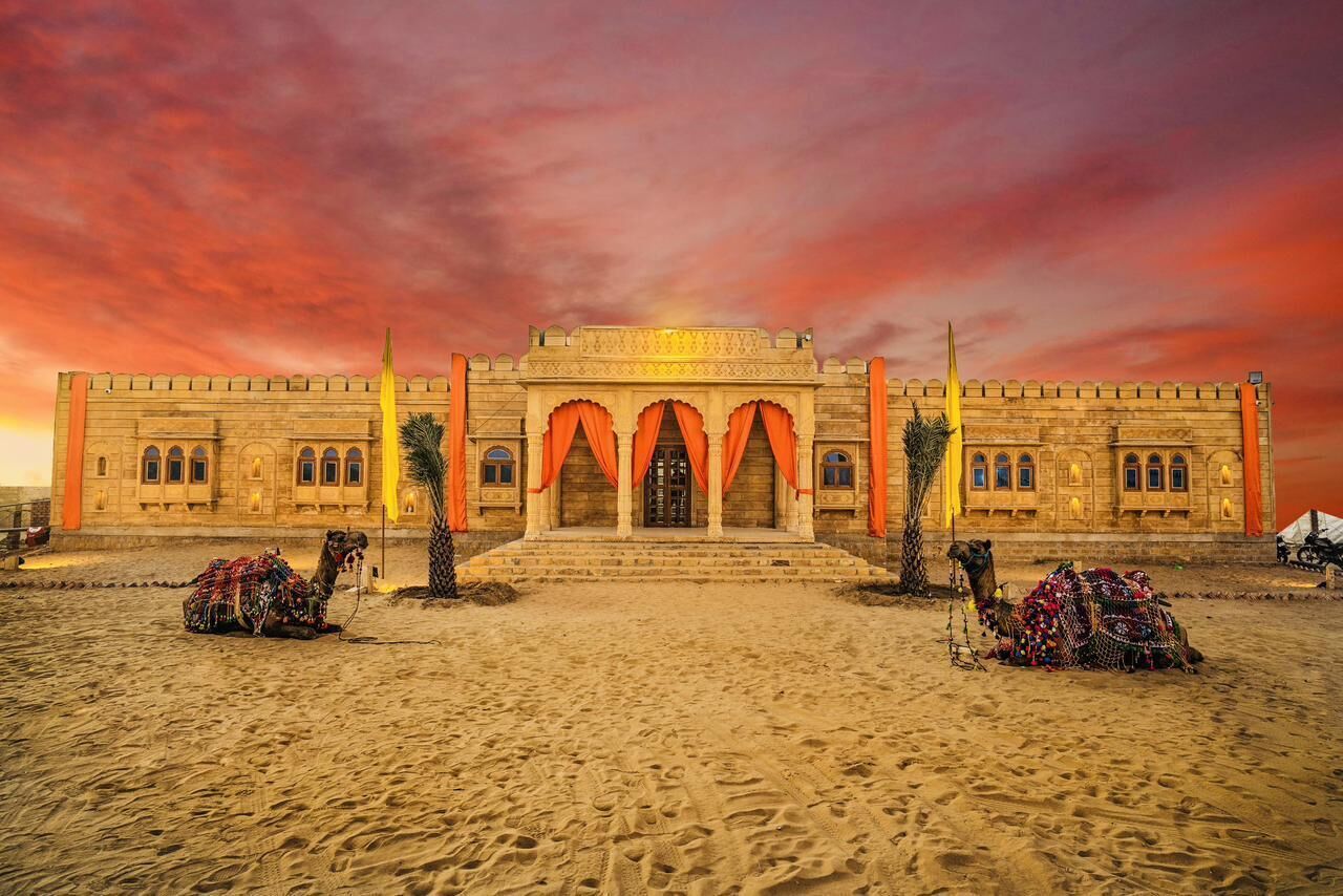A large, ornate building with a grand entrance, multiple arches, and a camel in the foreground.