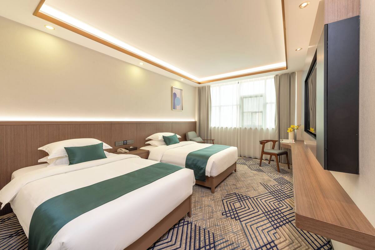 Une chambre d’hôtel avec deux lits, un bureau, une chaise, une télévision et une fenêtre avec des rideaux.