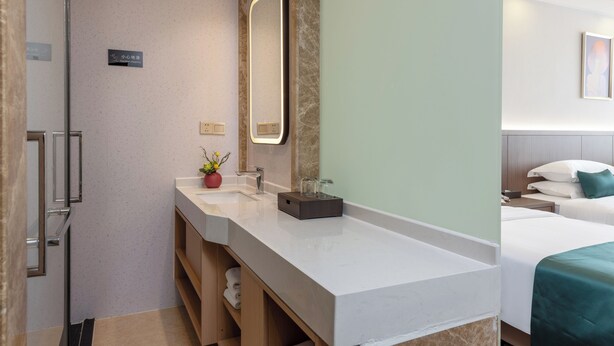 Une salle de bain d’hôtel moderne, dotée d’un grand miroir, de deux vasques et d’un espace douche.