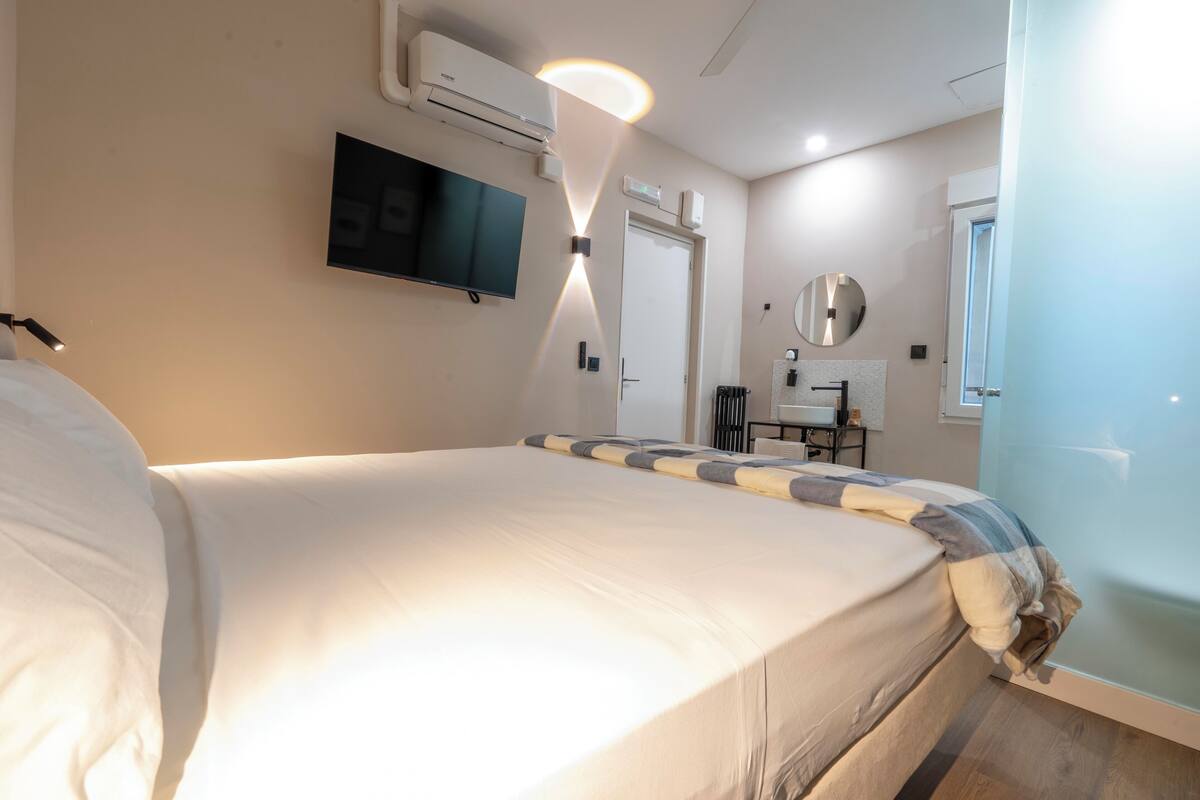 Hotelkamer met een bed, een aan de muur bevestigde televisie, een plafondventilator, een airconditioningsunit, een spiegel en een deur.