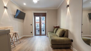 Un salon moderne avec un canapé, un téléviseur fixé au mur et une porte donnant sur un balcon extérieur.