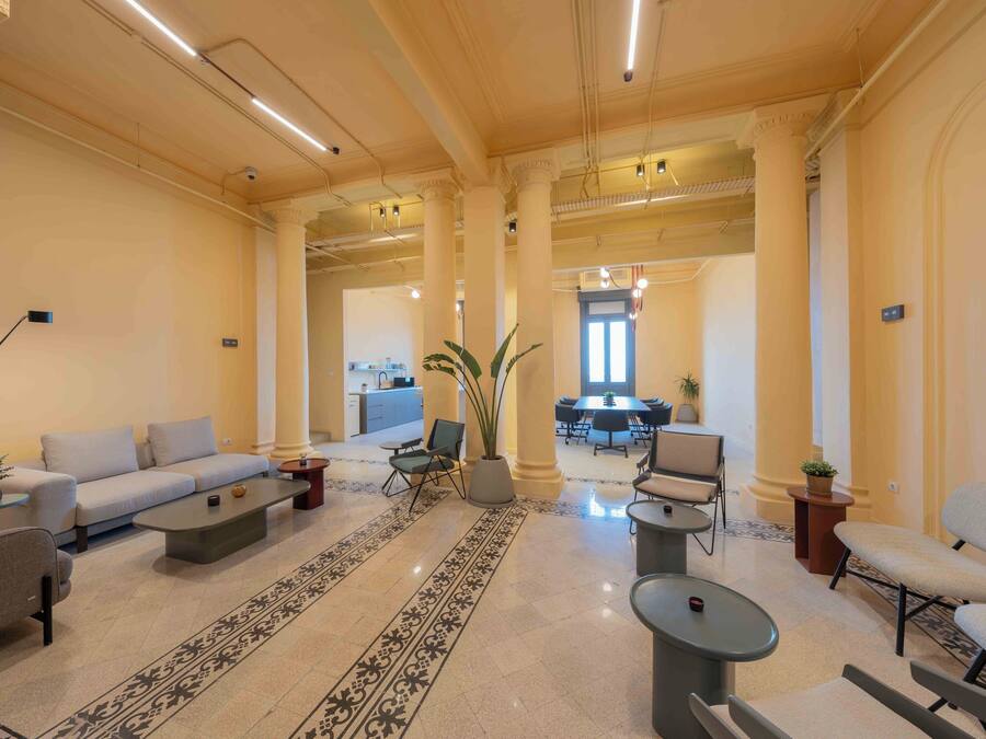 A spacious living area with a sofa, armchairs, a coffee table, and a dining table with chairs. There are potted plants and a large window providing natural light.