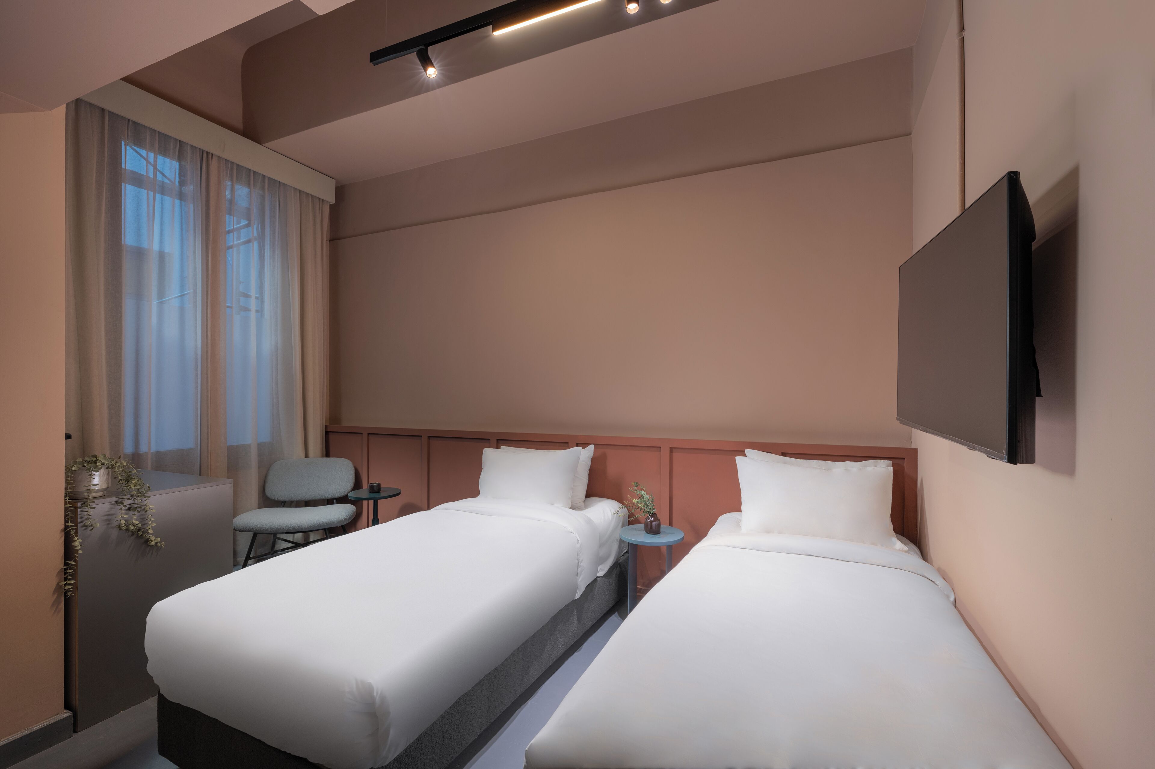Een hotelkamer met twee bedden, een aan de muur bevestigde televisie, een klein tafeltje en een stoel.