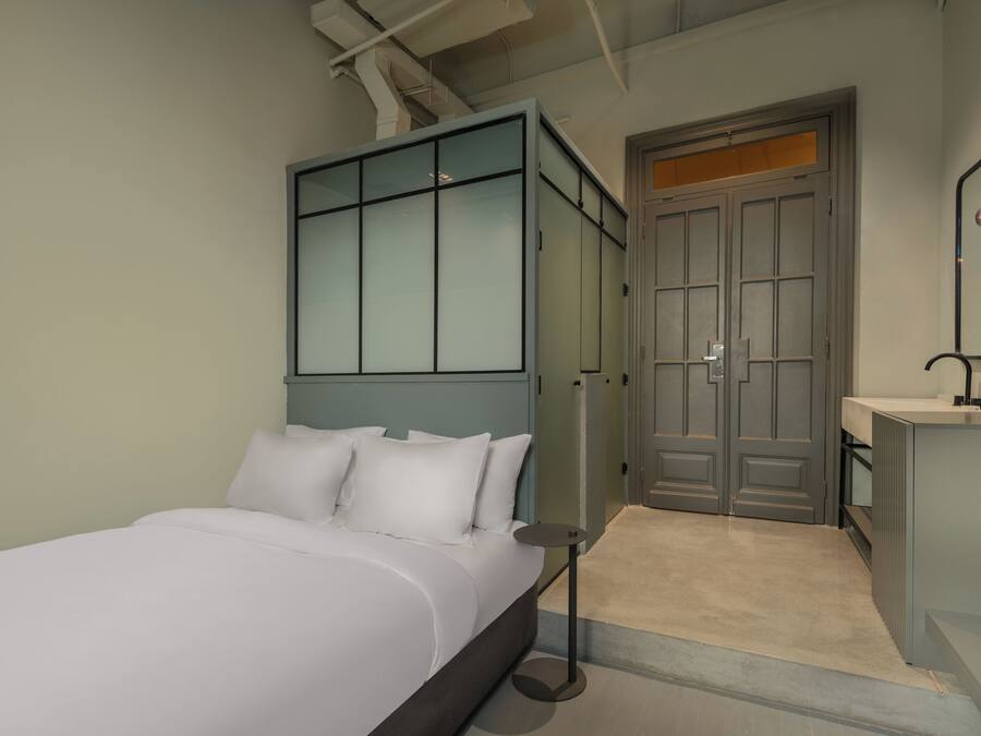 A modern bedroom with a bed, a bedside table, a mirror, and a door leading to a bathroom.