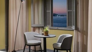 A balcony with two chairs, a small table with a plant, and a view of the sea at sunset. - Brassbell Grey Studio CornicheAlexandria (Alexandria)