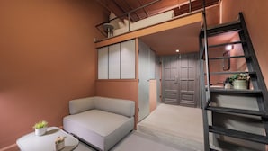 A compact room with a loft bed, a sofa, a small table with plants, and a staircase. - Brassbell Grey Studio CornicheAlexandria (Alexandria)