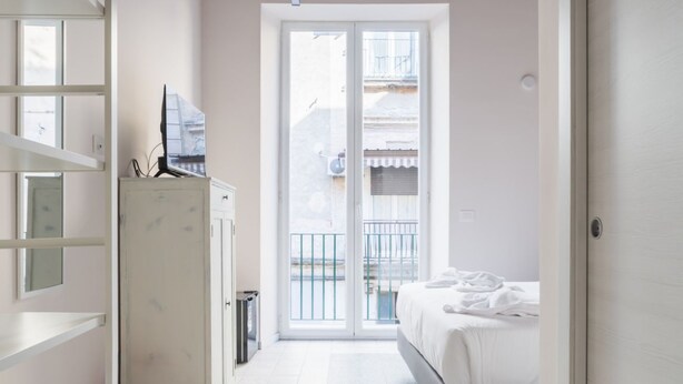 Et hotelværelse med en seng, et fjernsyn på et skab og en skydedør til en balkon.