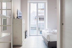 A hotel room with a bed, a television on a cabinet, and a sliding glass door to a balcony. - Tre santi apartments in city center (Napoli)