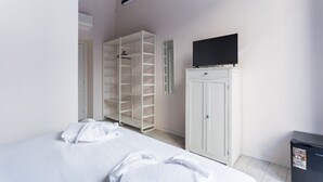 Et hotelværelse med seng, garderobeskab, fjernsyn og et lille køleskab.