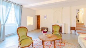 Una sala de estar con chimenea, una mesa redonda de madera, dos sillones verdes y un tapete estampado.