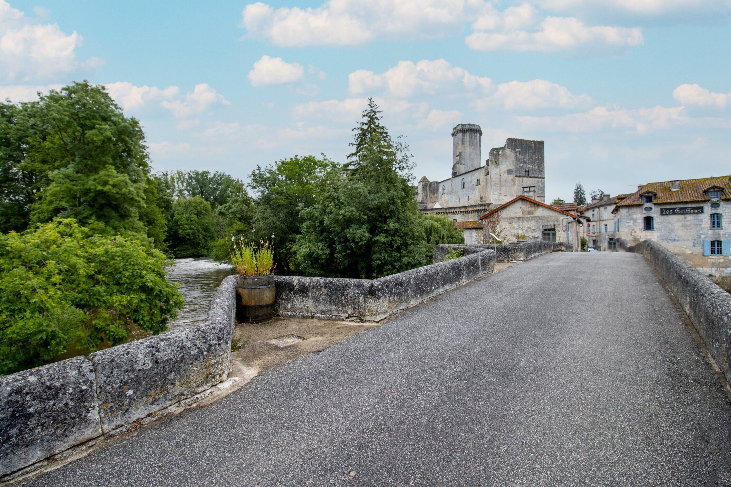 Un pont de pierre, avec une rivière d’un côté et un bâtiment ressemblant à un château, avec une tour en arrière-plan.
