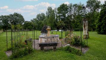 En fontän av sten med en bänk, omgiven av ett staket av metall, i ett grönområde som liknar en park.