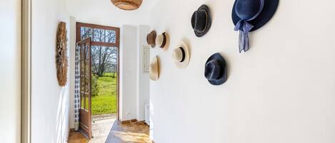 Ein Flur mit Holzboden, einer gewobenen Leuchte und einer Sammlung von Hüten an der Wand.